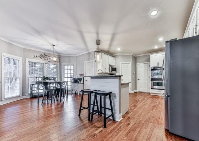 kitchen with a peninsula, white cabinetry, wood finished floors, stainless steel appliances, and a breakfast bar area