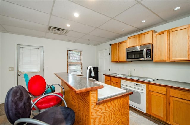 kitchen with an island with sink, sink, a kitchen breakfast bar, a drop ceiling, and white appliances