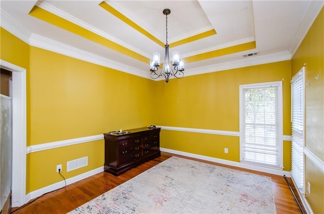 empty room featuring crown molding, an inviting chandelier, a raised ceiling, and dark wood-type flooring