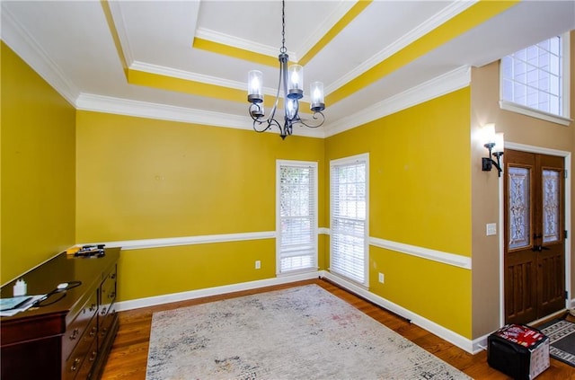 interior space with a notable chandelier, a tray ceiling, dark wood-type flooring, and ornamental molding