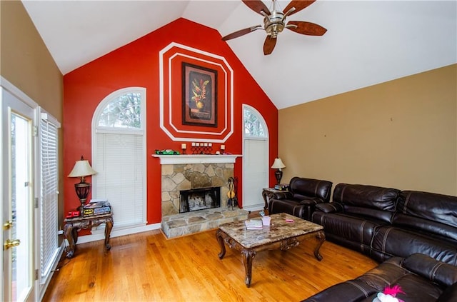 living room with hardwood / wood-style flooring, lofted ceiling, a stone fireplace, and ceiling fan