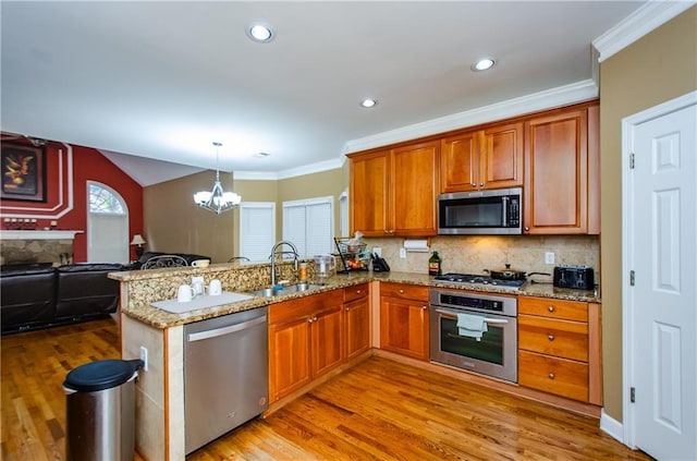 kitchen with appliances with stainless steel finishes, decorative light fixtures, sink, backsplash, and kitchen peninsula