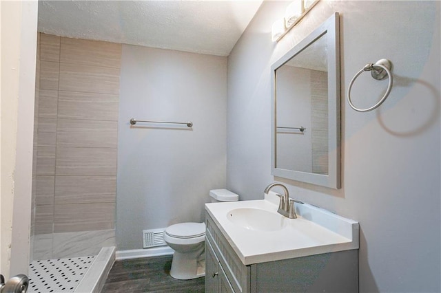 bathroom featuring toilet, vanity, hardwood / wood-style floors, a textured ceiling, and a tile shower