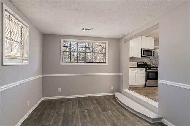 kitchen featuring tasteful backsplash, white cabinetry, appliances with stainless steel finishes, dark wood-type flooring, and a textured ceiling