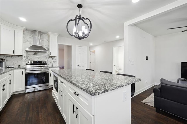 kitchen with dark hardwood / wood-style flooring, a kitchen island, stainless steel electric stove, wall chimney range hood, and white cabinetry