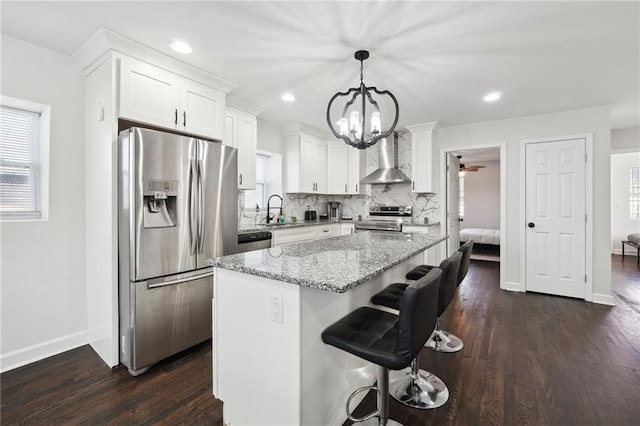 kitchen with wall chimney range hood, white cabinets, decorative light fixtures, and appliances with stainless steel finishes