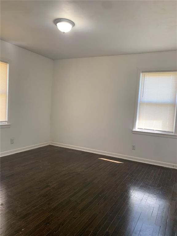 empty room with a wealth of natural light, baseboards, and dark wood-style floors