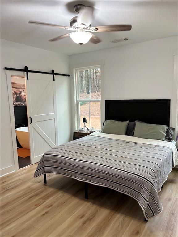 bedroom featuring wood-type flooring, a barn door, and ceiling fan