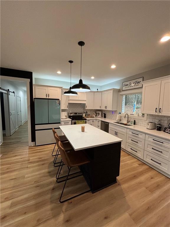 kitchen with a center island, hanging light fixtures, a barn door, a breakfast bar area, and appliances with stainless steel finishes