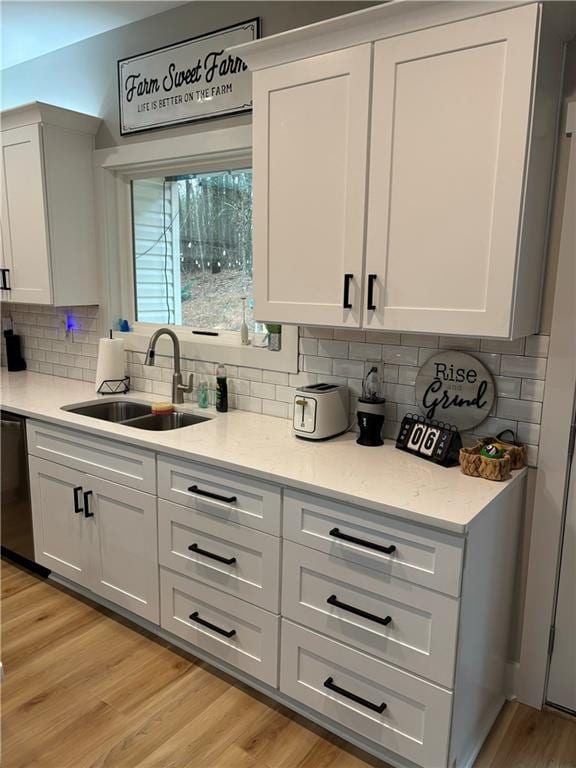 kitchen with backsplash, white cabinets, sink, light hardwood / wood-style flooring, and stainless steel dishwasher