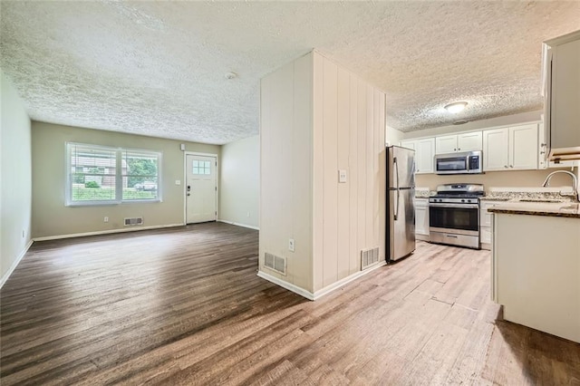 kitchen featuring a textured ceiling, appliances with stainless steel finishes, light hardwood / wood-style floors, sink, and white cabinetry