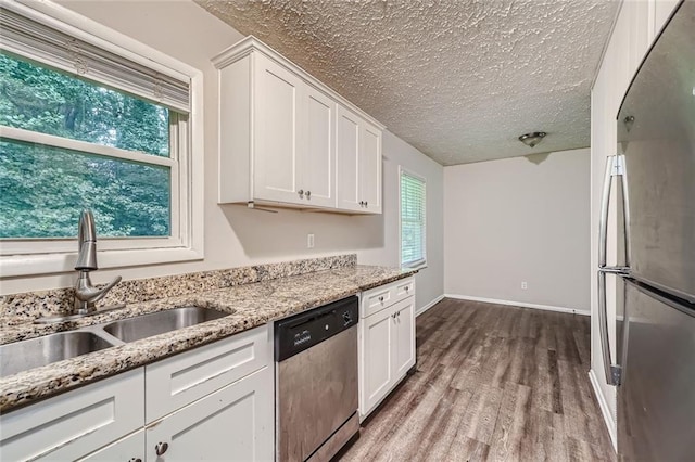 kitchen featuring hardwood / wood-style floors, white cabinetry, stainless steel appliances, sink, and light stone countertops