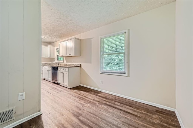 kitchen with a textured ceiling, light hardwood / wood-style flooring, dishwasher, light stone counters, and white cabinets