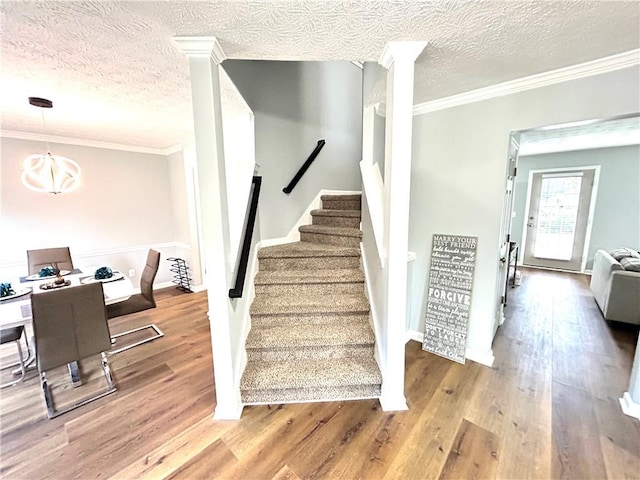 stairs with ornate columns, a chandelier, a textured ceiling, ornamental molding, and hardwood / wood-style flooring