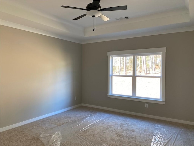 carpeted empty room with a raised ceiling and ceiling fan