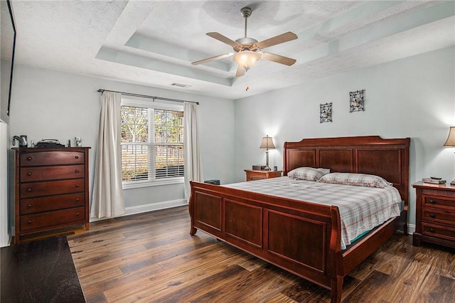 bedroom featuring a ceiling fan, a tray ceiling, a textured ceiling, wood finished floors, and baseboards