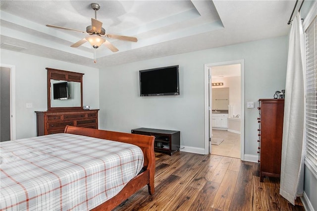 bedroom featuring connected bathroom, a tray ceiling, baseboards, and wood finished floors