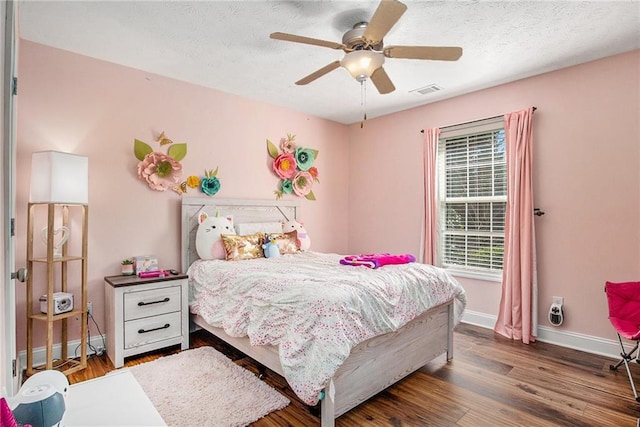 bedroom featuring visible vents, a textured ceiling, baseboards, and wood finished floors