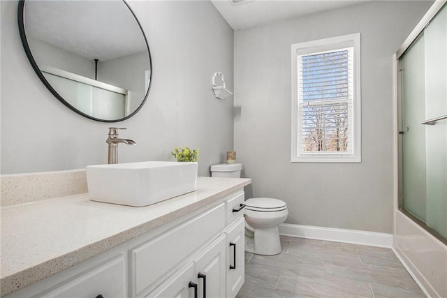 bathroom with vanity, toilet, baseboards, and combined bath / shower with glass door