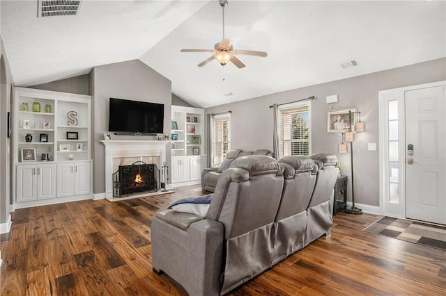 living area with visible vents, lofted ceiling, a lit fireplace, and wood finished floors