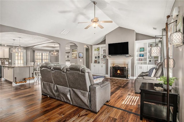 living room featuring built in features, dark wood-style floors, a fireplace with flush hearth, arched walkways, and vaulted ceiling