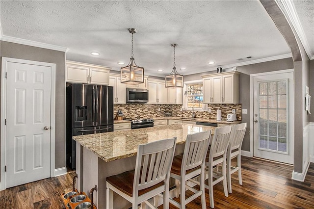 kitchen with dark wood finished floors, a center island, stainless steel appliances, arched walkways, and light stone countertops