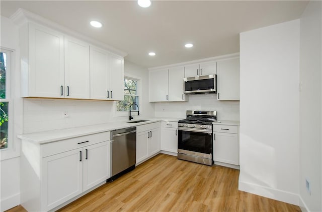 kitchen featuring white cabinetry, sink, tasteful backsplash, light hardwood / wood-style floors, and appliances with stainless steel finishes