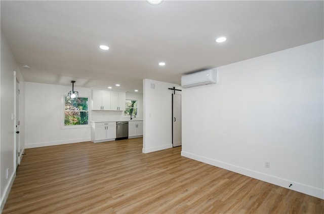 unfurnished living room with a barn door, light hardwood / wood-style floors, a wall mounted AC, and sink