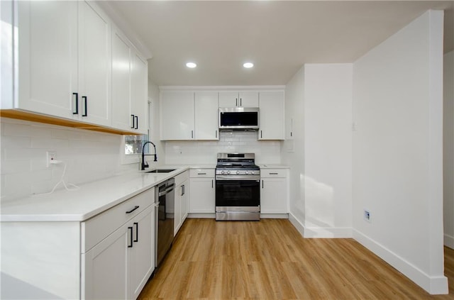 kitchen featuring sink, stainless steel appliances, light hardwood / wood-style flooring, backsplash, and white cabinets