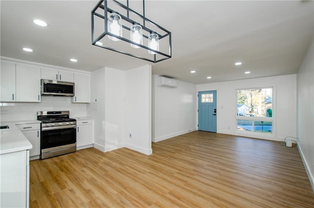 kitchen with appliances with stainless steel finishes, tasteful backsplash, a wall mounted AC, decorative light fixtures, and white cabinetry