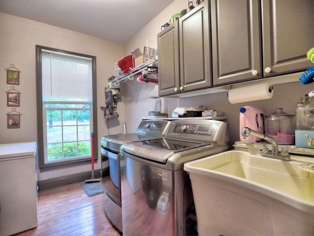 laundry room with a sink, cabinet space, washer and dryer, and light wood-style flooring