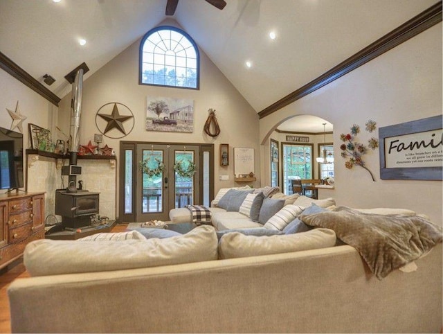living room featuring ceiling fan, french doors, arched walkways, a wood stove, and high vaulted ceiling