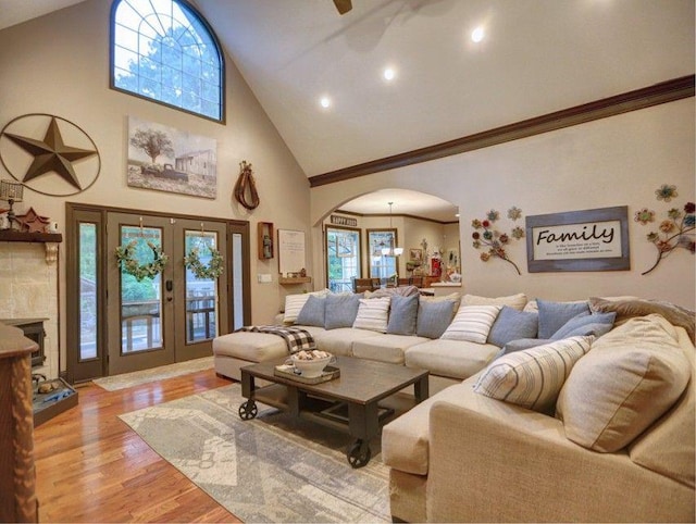 living room with ceiling fan, arched walkways, high vaulted ceiling, light wood finished floors, and ornamental molding