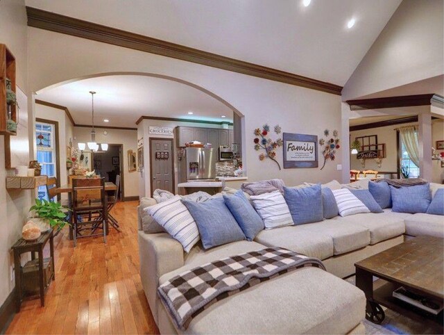 living room with arched walkways, ornamental molding, and light wood finished floors