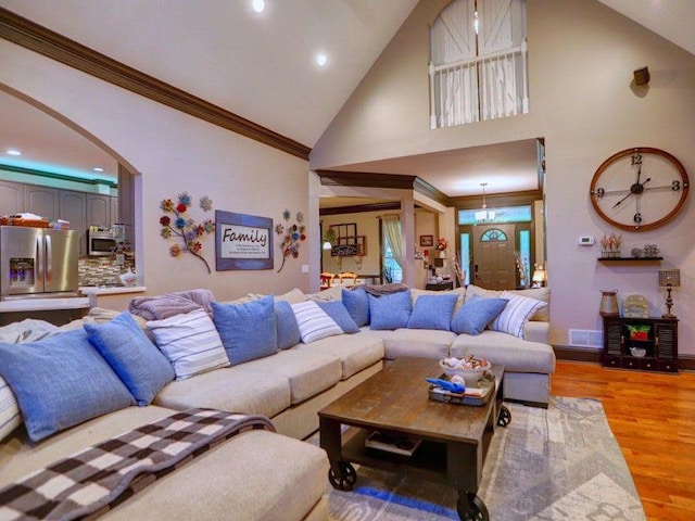 living area featuring crown molding, arched walkways, high vaulted ceiling, recessed lighting, and light wood-style flooring
