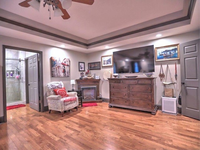 living area with light wood-style floors, recessed lighting, ceiling fan, and a tray ceiling