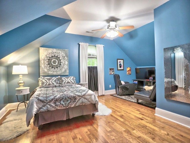bedroom featuring a ceiling fan, visible vents, vaulted ceiling, wood finished floors, and baseboards