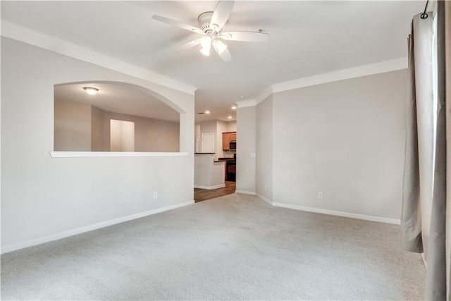 empty room with arched walkways, crown molding, light colored carpet, a ceiling fan, and baseboards