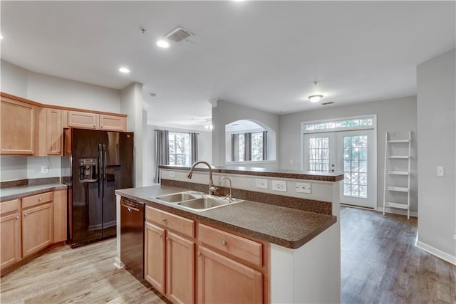 kitchen with black appliances, dark countertops, a sink, and light wood-style floors