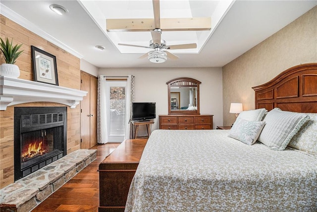 bedroom with a ceiling fan, beamed ceiling, dark wood-style flooring, and a stone fireplace