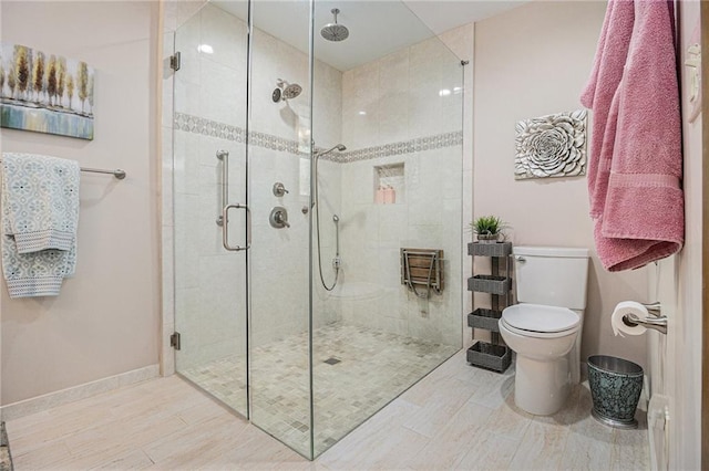 bathroom featuring toilet, a shower stall, and baseboards