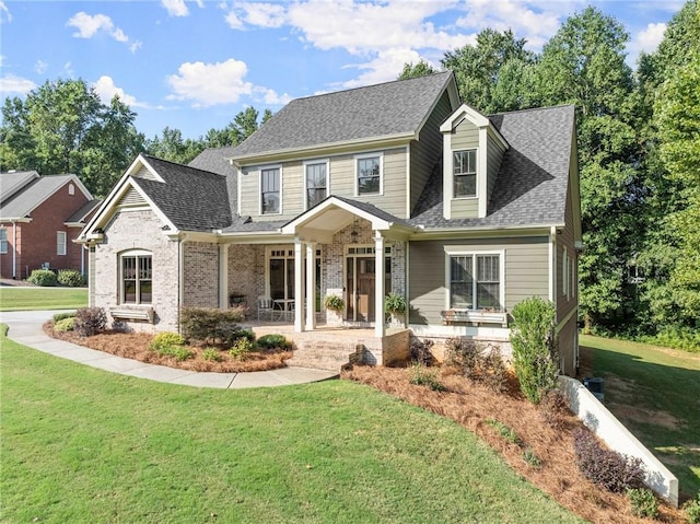view of front of home with a shingled roof, covered porch, a front yard, and brick siding