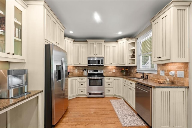 kitchen featuring dark stone counters, tasteful backsplash, a sink, light wood-style flooring, and appliances with stainless steel finishes