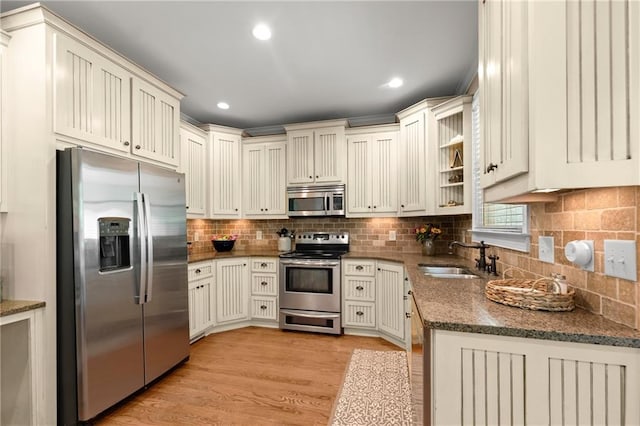 kitchen featuring backsplash, dark stone countertops, stainless steel appliances, and a sink