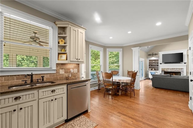 kitchen with stainless steel dishwasher, a sink, dark stone counters, crown molding, and a lit fireplace