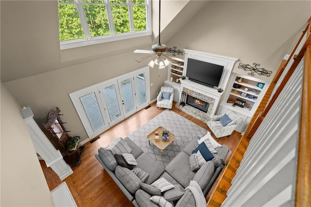 living room featuring a towering ceiling, wood finished floors, visible vents, a ceiling fan, and a fireplace