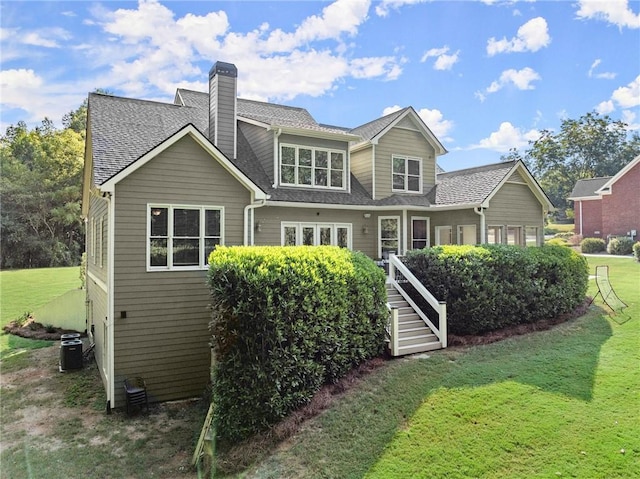 rear view of property with a lawn, a shingled roof, a chimney, and central AC unit