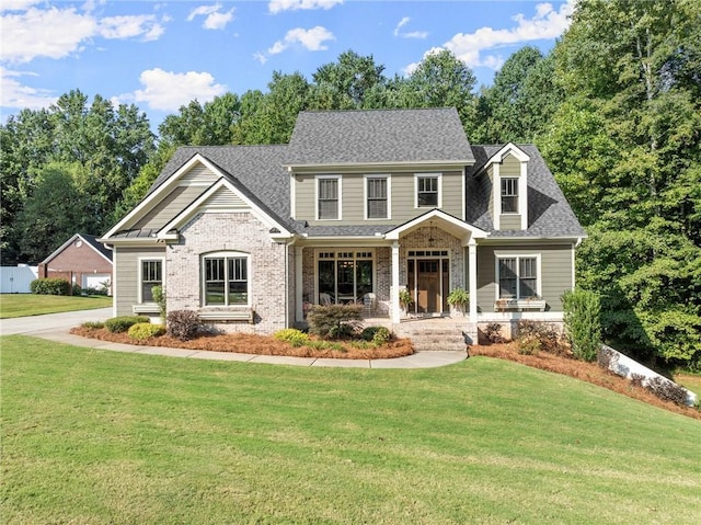 craftsman-style house featuring brick siding, a front yard, a shingled roof, and covered porch