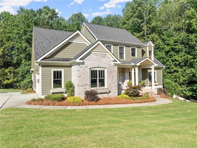 craftsman house featuring a porch, brick siding, a front yard, and roof with shingles