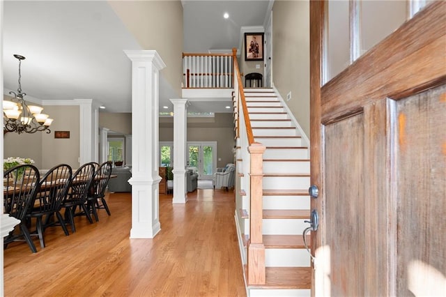 stairs featuring an inviting chandelier, a towering ceiling, wood finished floors, and ornate columns